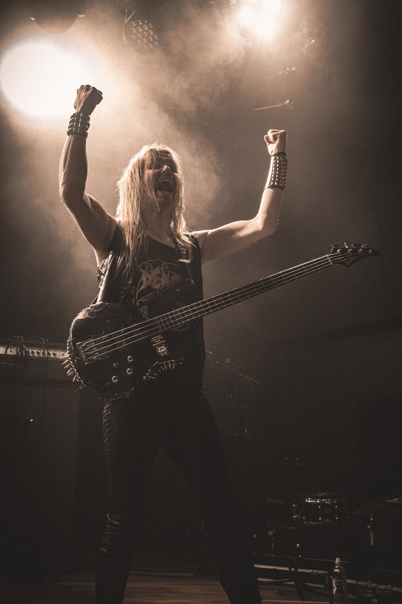 Bassist med knyttede never og piggarmbånd på scenen i røyk og lys