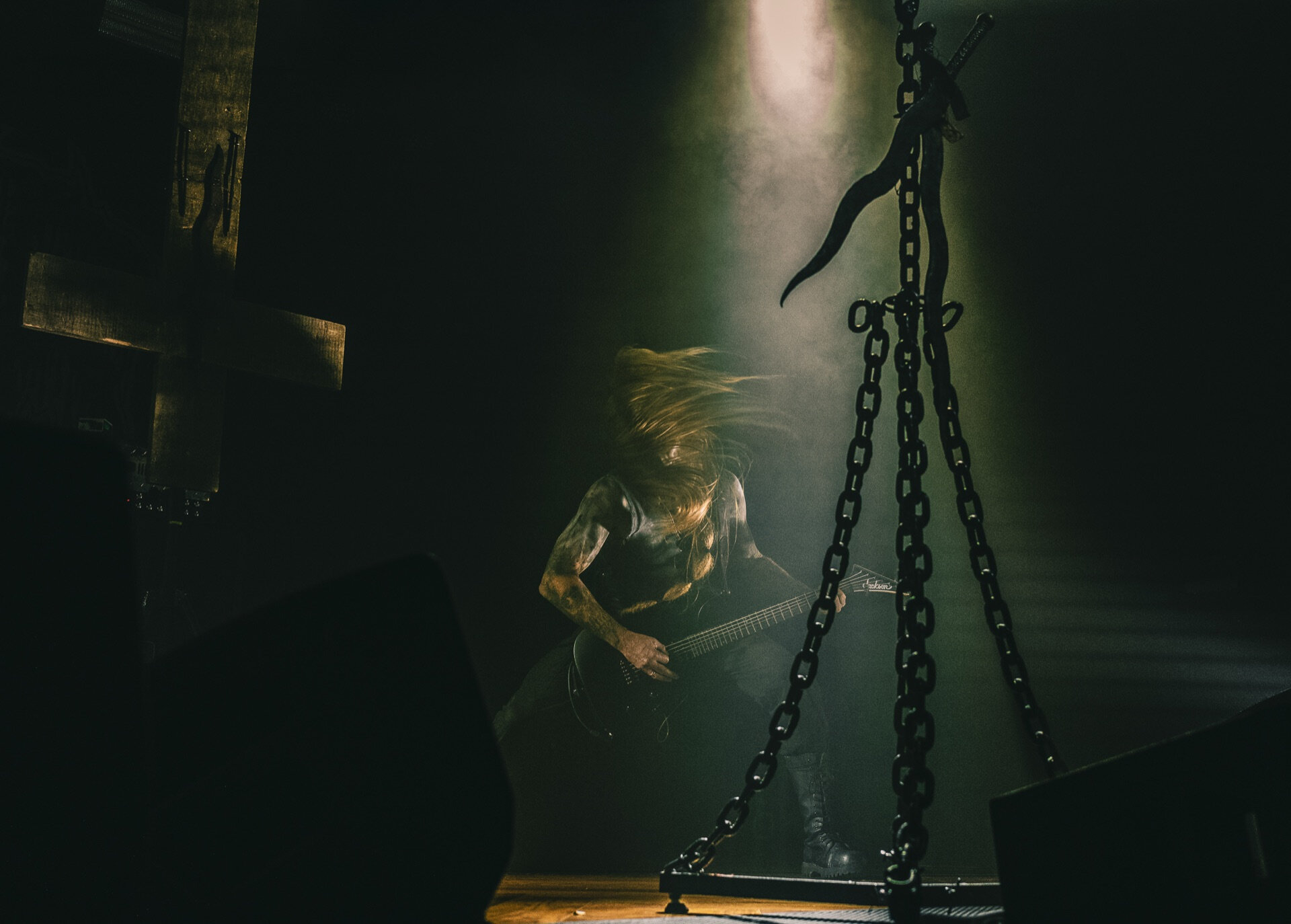 Gitarist med langt hår headbanger på mørk scene med lenker og kors som rekvisitt