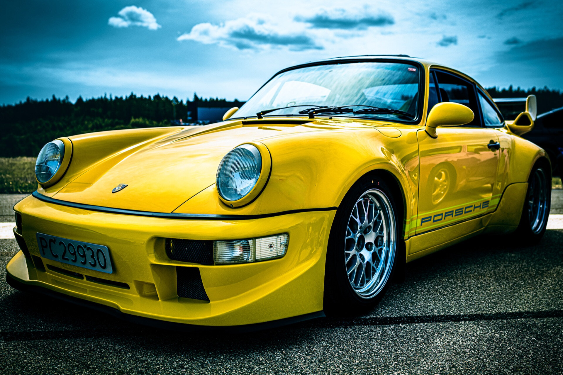 Gul Porsche 911 fotografert skrått forfra på asfaltert bane under skyet himmel