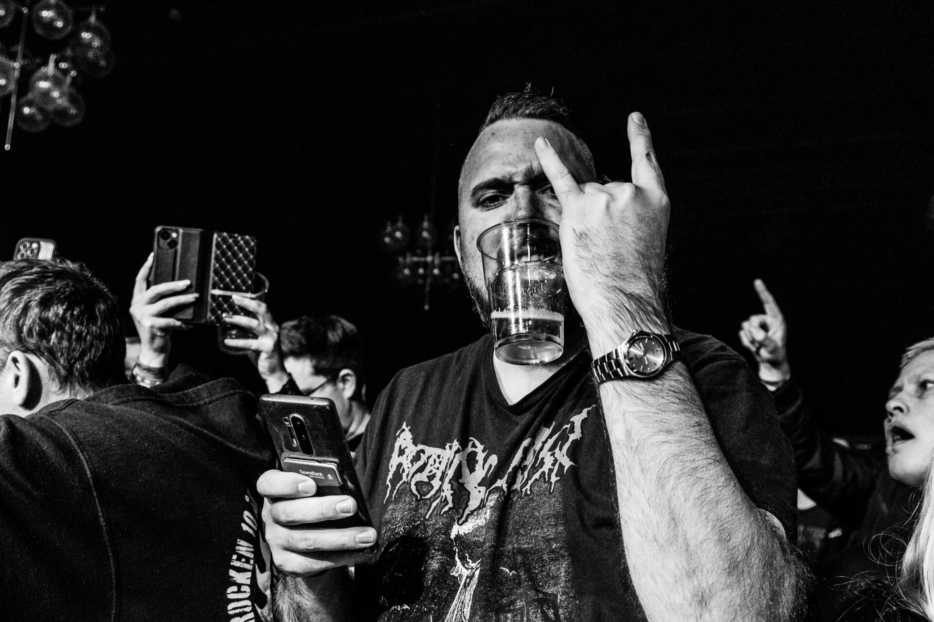 Svart-hvitt nærbilde av publikummer som viser hornsymbol med hånden på konsert