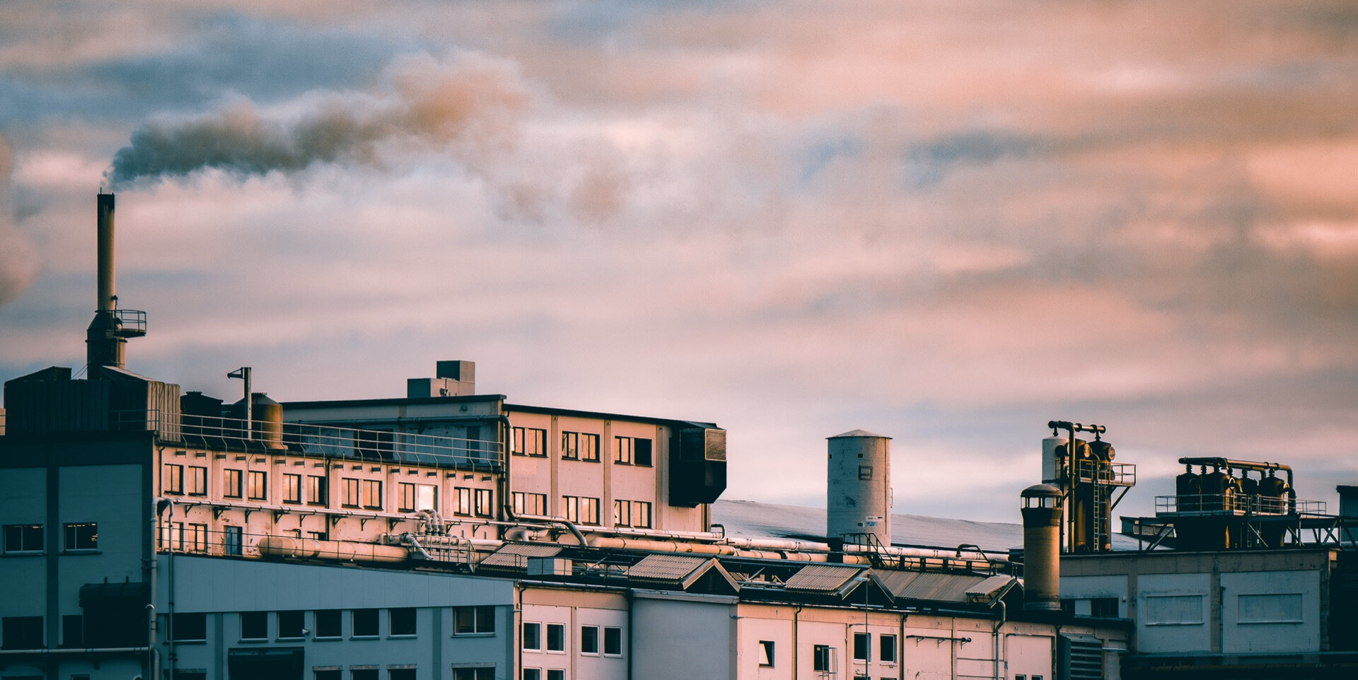 Industribygning med rykende pipe mot rosa og blå kveldshimmel