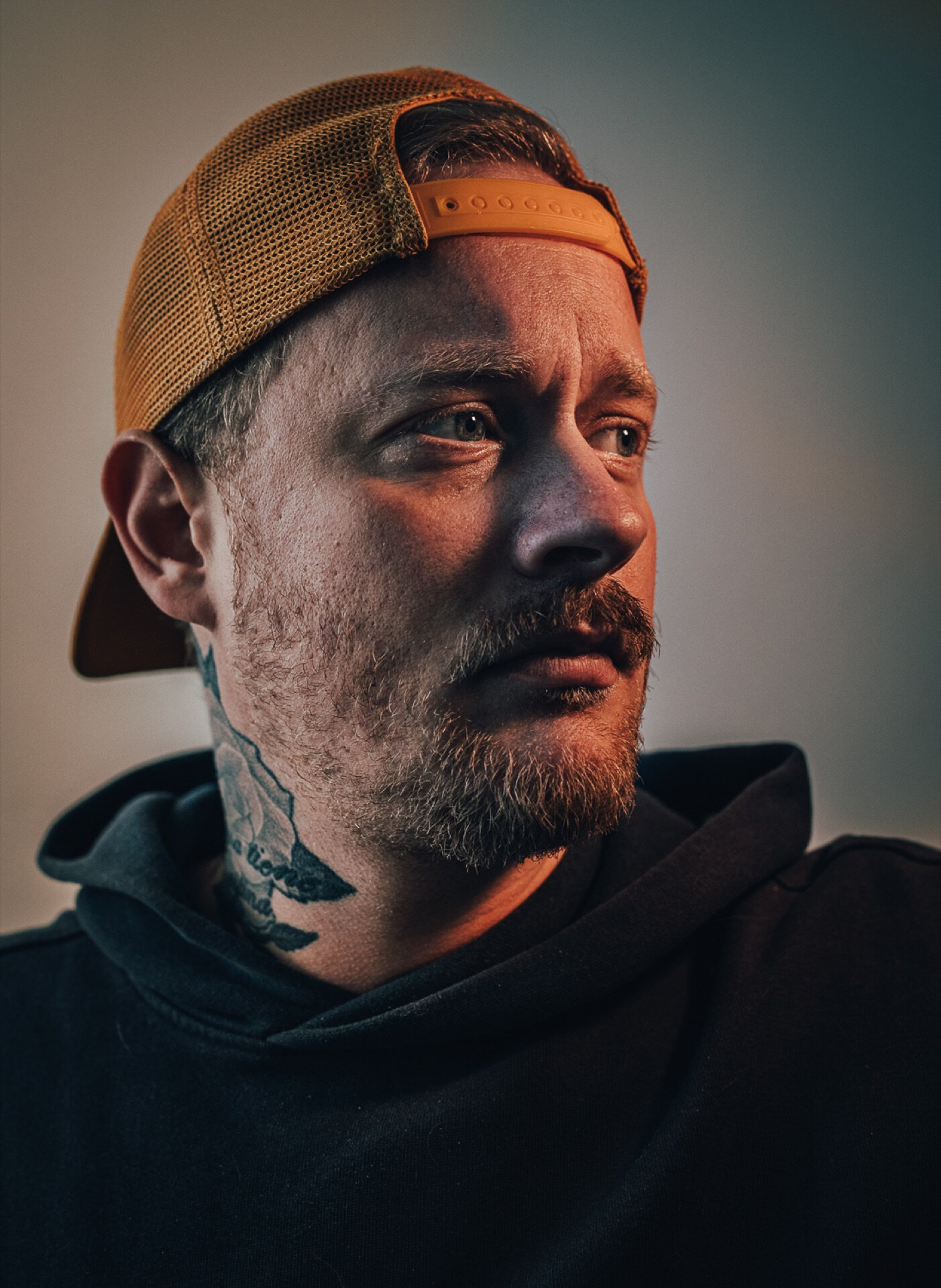 Portrett av mann i oransje caps med nakketatovering i fargerikt lys