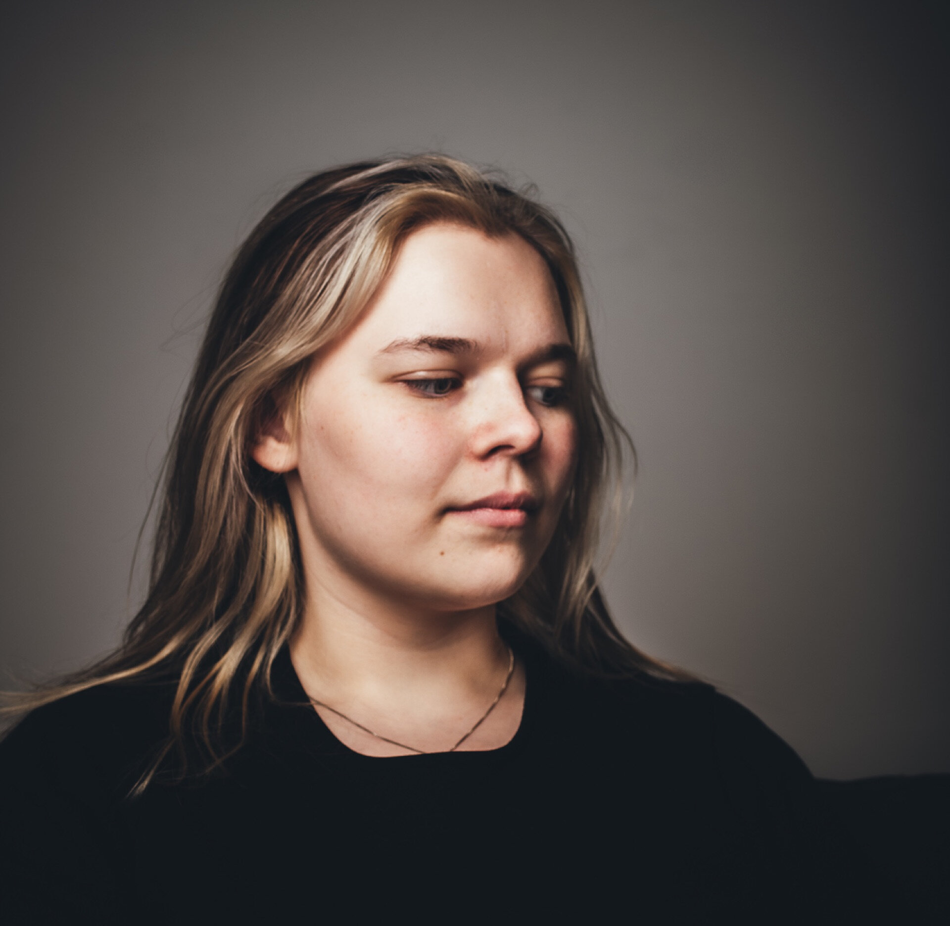 Portrett av lyshåret kvinne som ser nedover mot grå bakgrunn