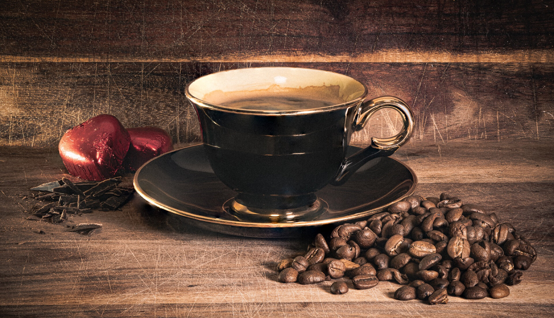 Kaffekopp på gullkantet fat med kaffebønner og sjokoladehjerter i stilleben